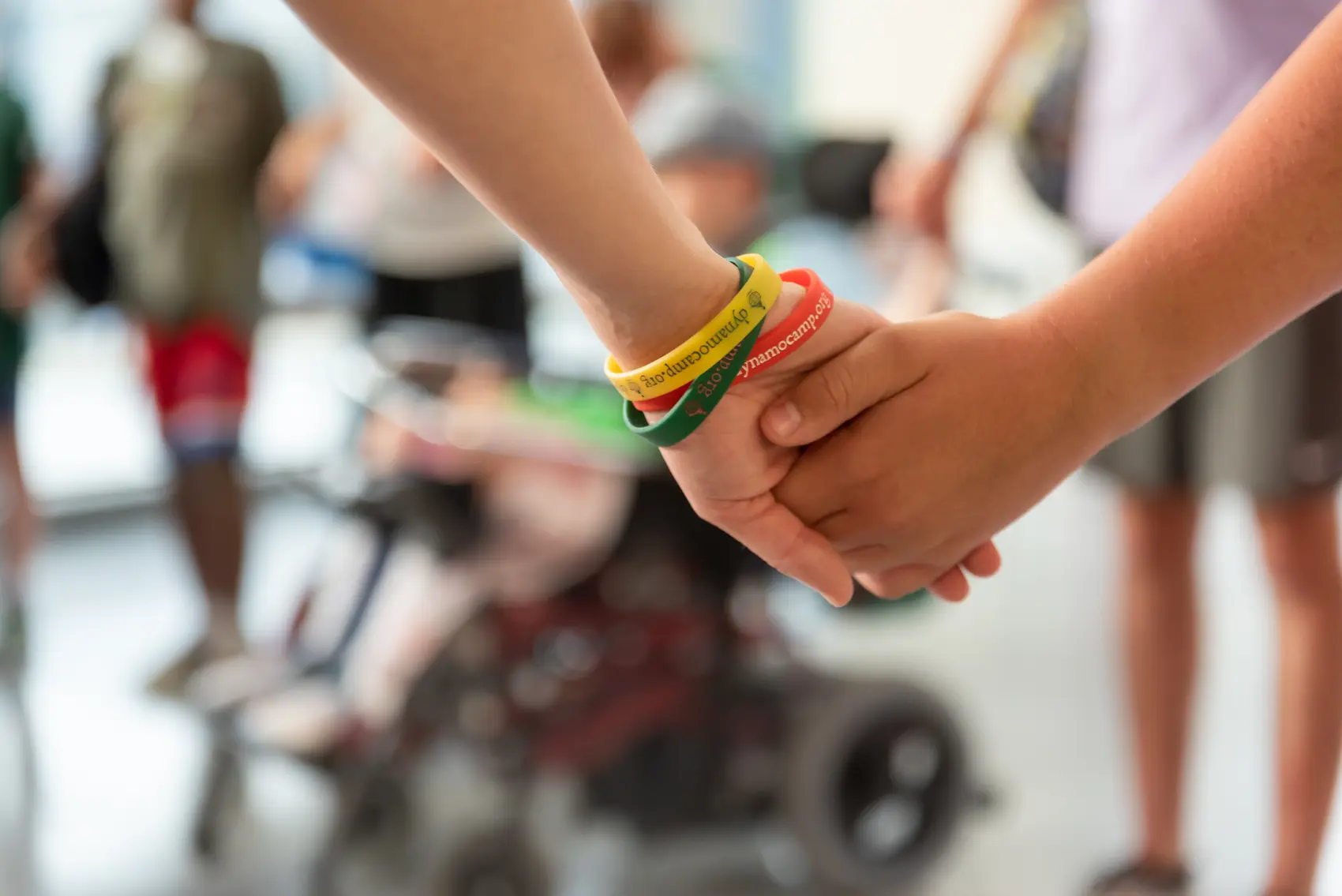 Due mani unite con braccialetti Dynamo Camp, un gesto di sostegno che aiuta a regalare felicità ai bambini con malattie gravi o croniche.